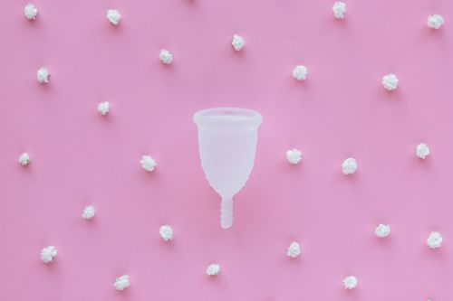 Free Eco-friendly menstrual cup on a pastel pink background with decorative elements. Stock Photo