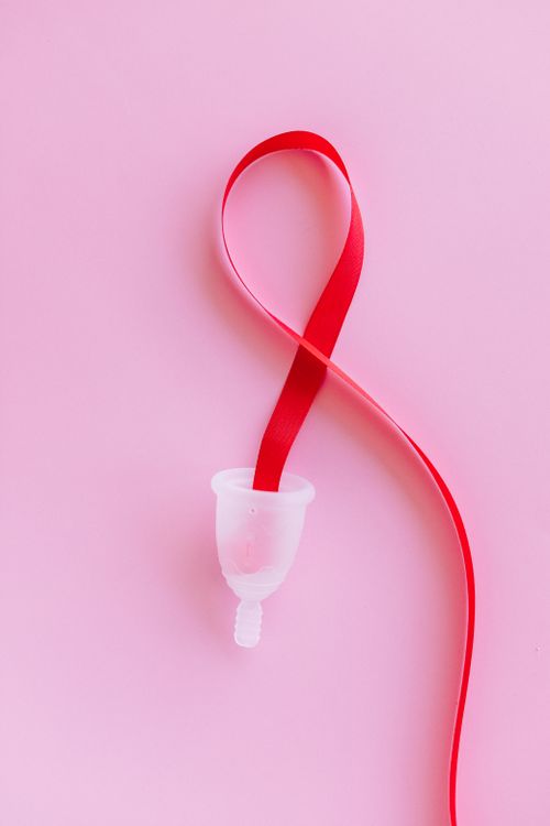 Free A menstrual cup with a red ribbon on a pink surface symbolizing feminine hygiene. Stock Photo