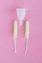 Menstrual cup and tampons arranged on a pink surface for feminine hygiene.