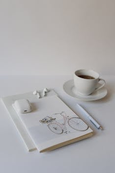 A minimalist still life featuring a coffee cup, notebook, pen, and wireless earphones.