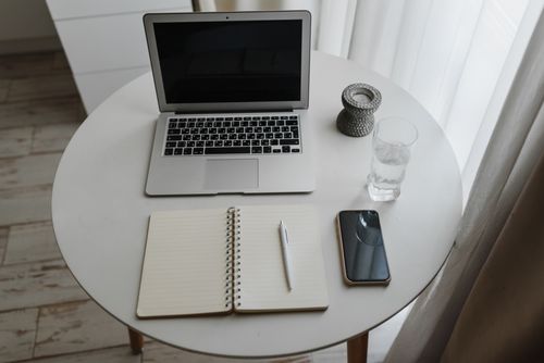 Free A neat workspace featuring a laptop, notebook, pen, and smartphone on a round table indoors. Stock Photo
