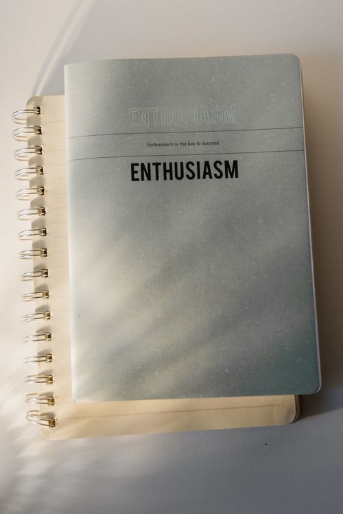 Free Top view of a minimalist notebook with 'Enthusiasm' printed on the cover, on a white background. Stock Photo