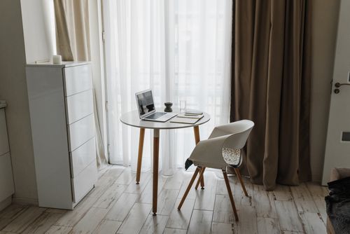 Free Minimalist home office setup with a laptop, table, and chair by a window for a serene workspace. Stock Photo