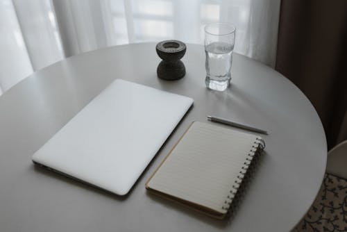 桌上的透明水杯旁邊的白色筆記本
