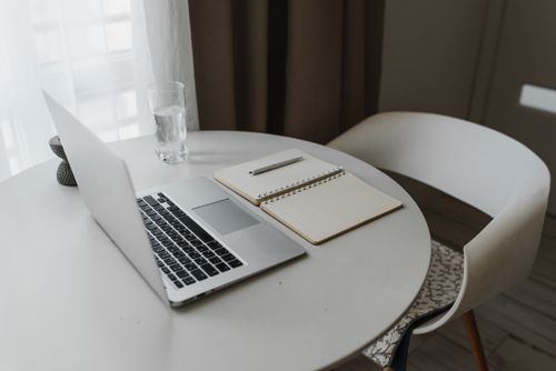 Free A serene home office setup with a laptop, notebook, pen, and glass of water on a round table. Stock Photo