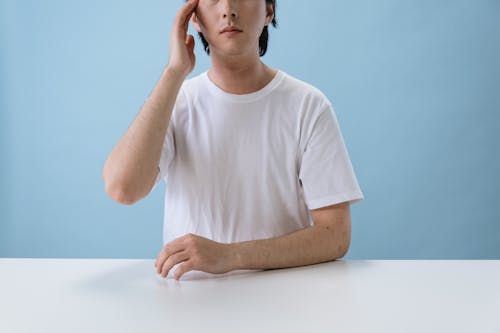 Free Man in White T-shirt Sitting and Touching Head Stock Photo