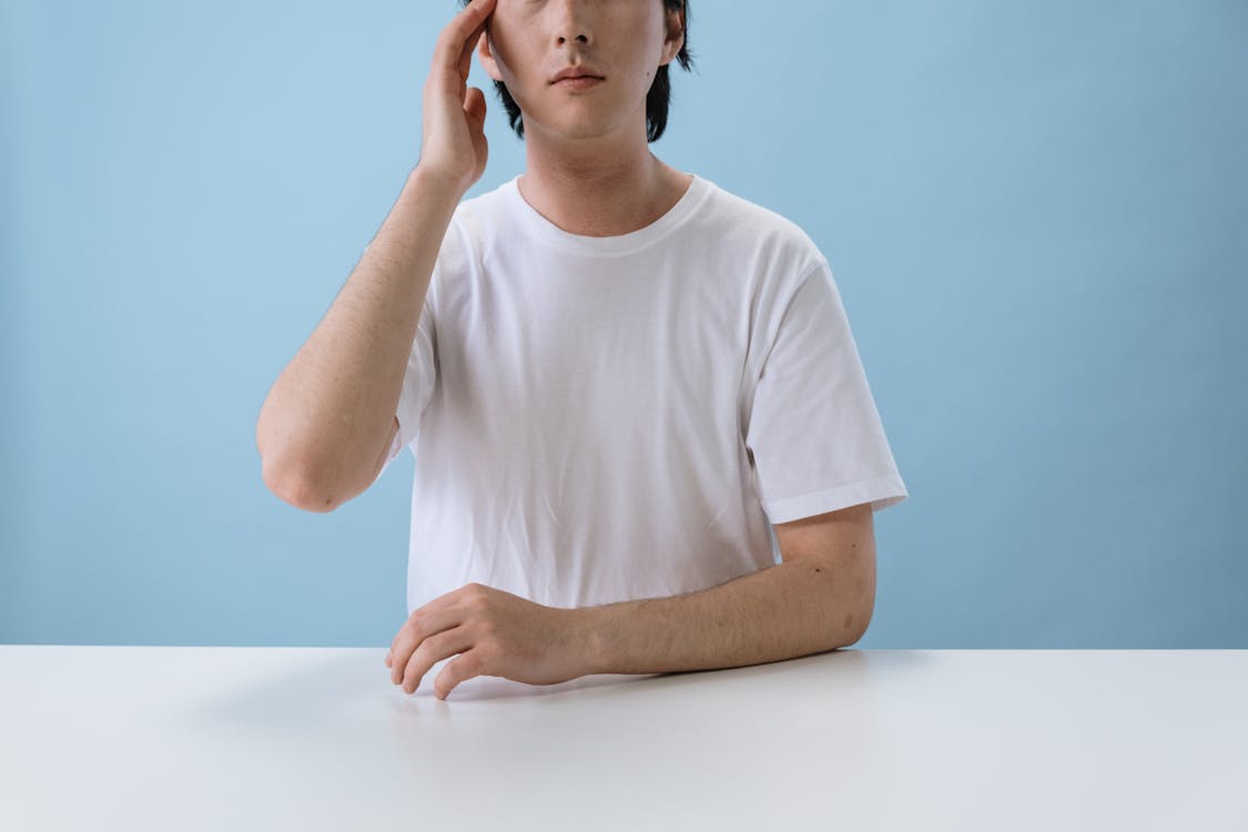 Man in White T-shirt Sitting and Touching Head