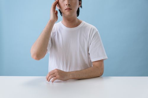 Free A man in a blank white t-shirt sits pensively against a blue background. Stock Photo