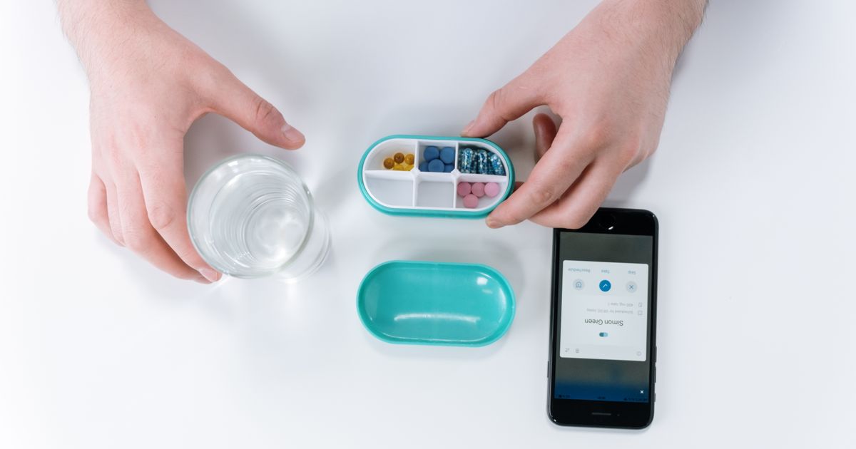 Overhead view of hands using a smartphone app beside a pill organizer.