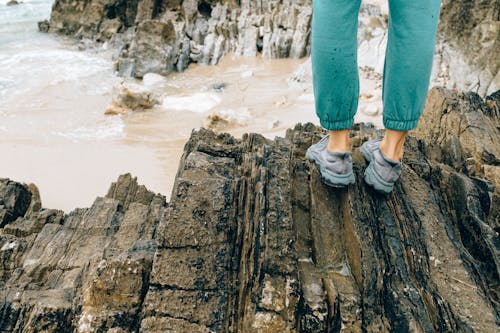 Woman in Gray Hiking Sneakers Standing on Brown Rock