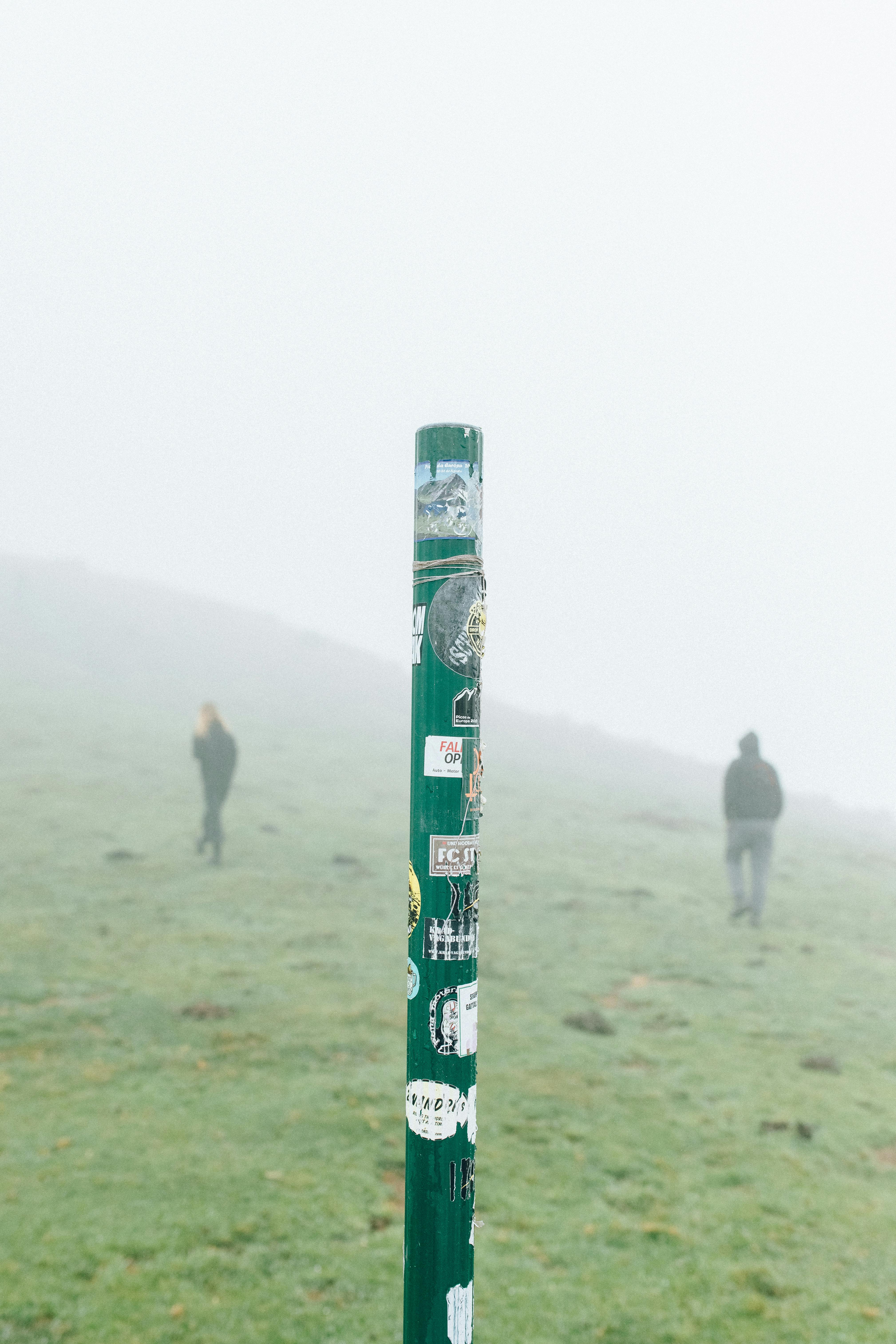 雾气缭绕的风景中，一根贴有贴纸的杆子立在背景里，两个人在徒步旅行