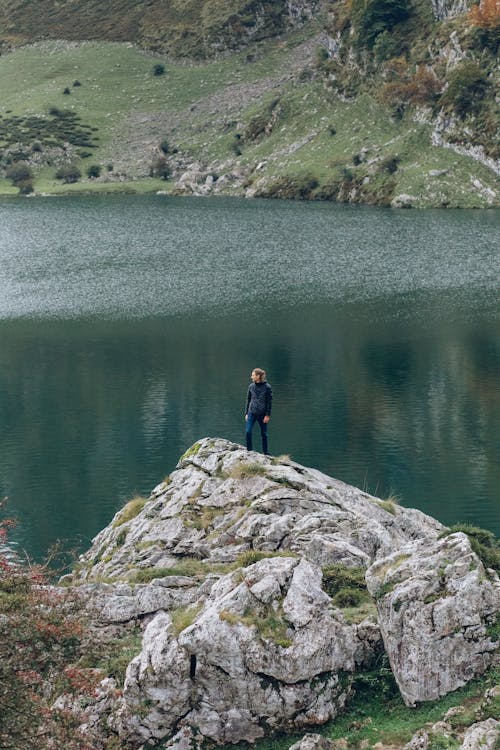 Man in Black Jacket Standing on Rock Near Lake