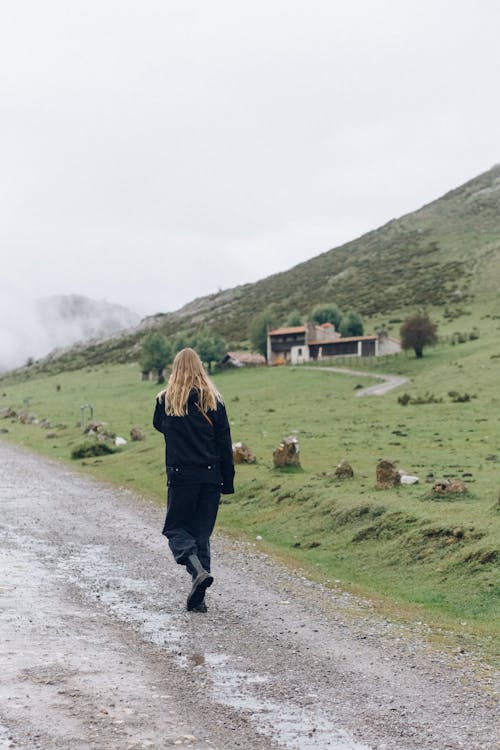 a Person in Black Coat Walking on Gray Dirt Road