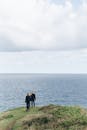夫妇在多云的天空下沿着草木悬崖俯瞰大海享受宁静的散步