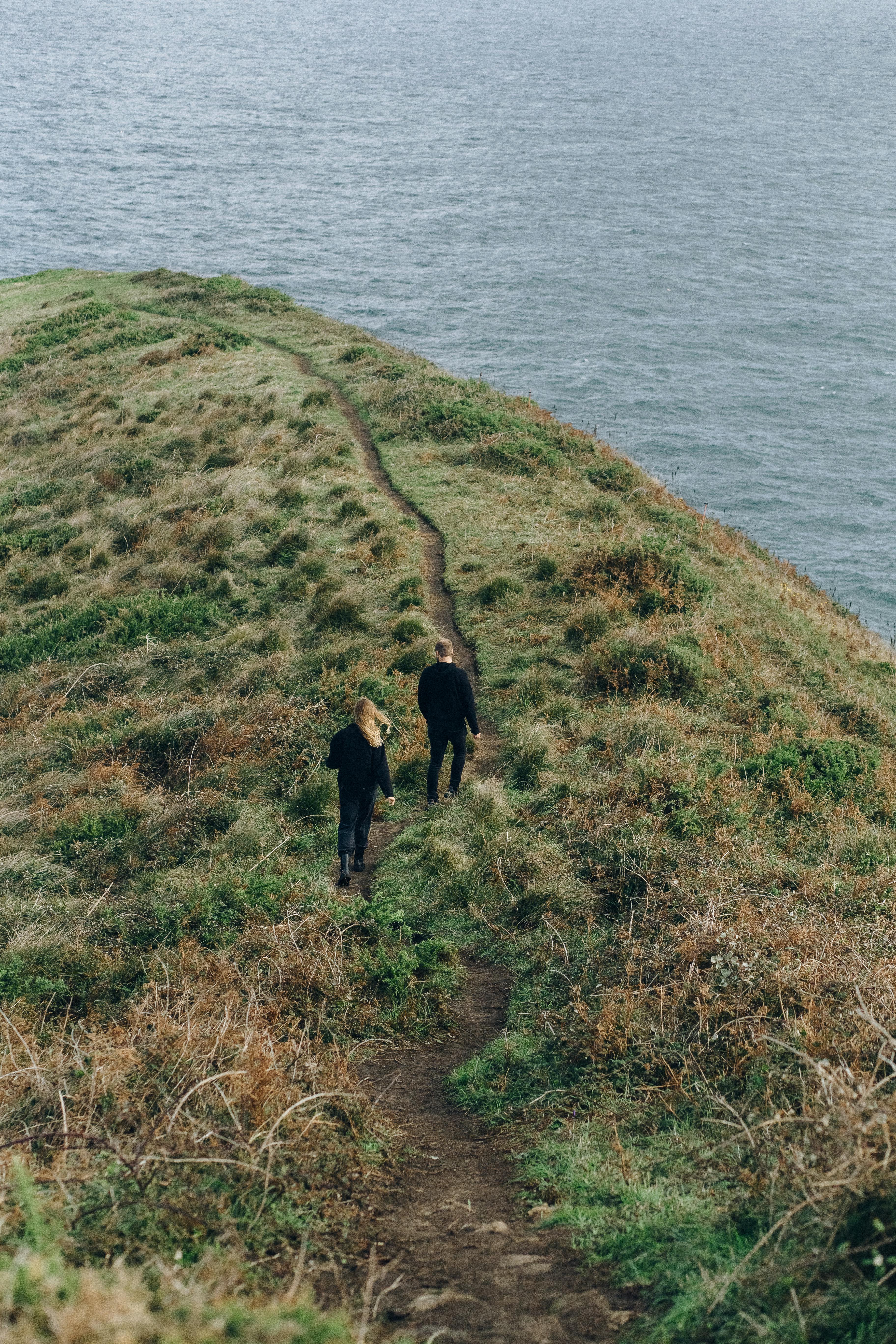 man in black jacket walking on green grass field near body of water