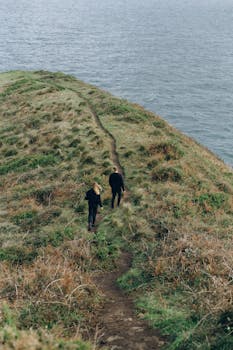 在多云的天空下，两名徒步旅行者行走在海边风景优美的沿海悬崖小道上