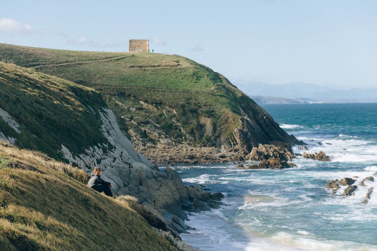 Person Sitting On A Cliff Edge Looking At Sea