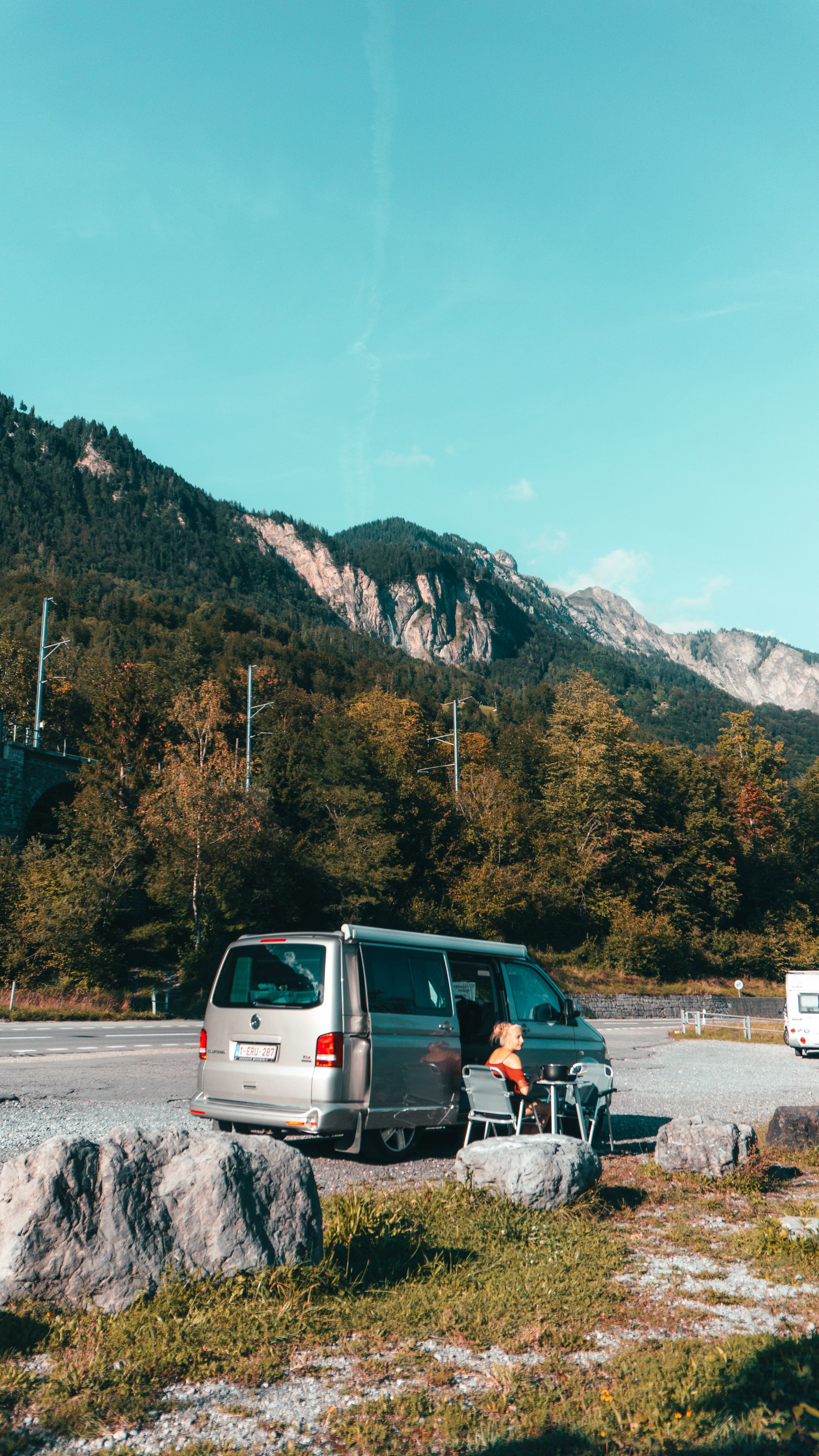 Camping in a van amidst stunning Swiss mountains with clear blue sky and lush greenery.