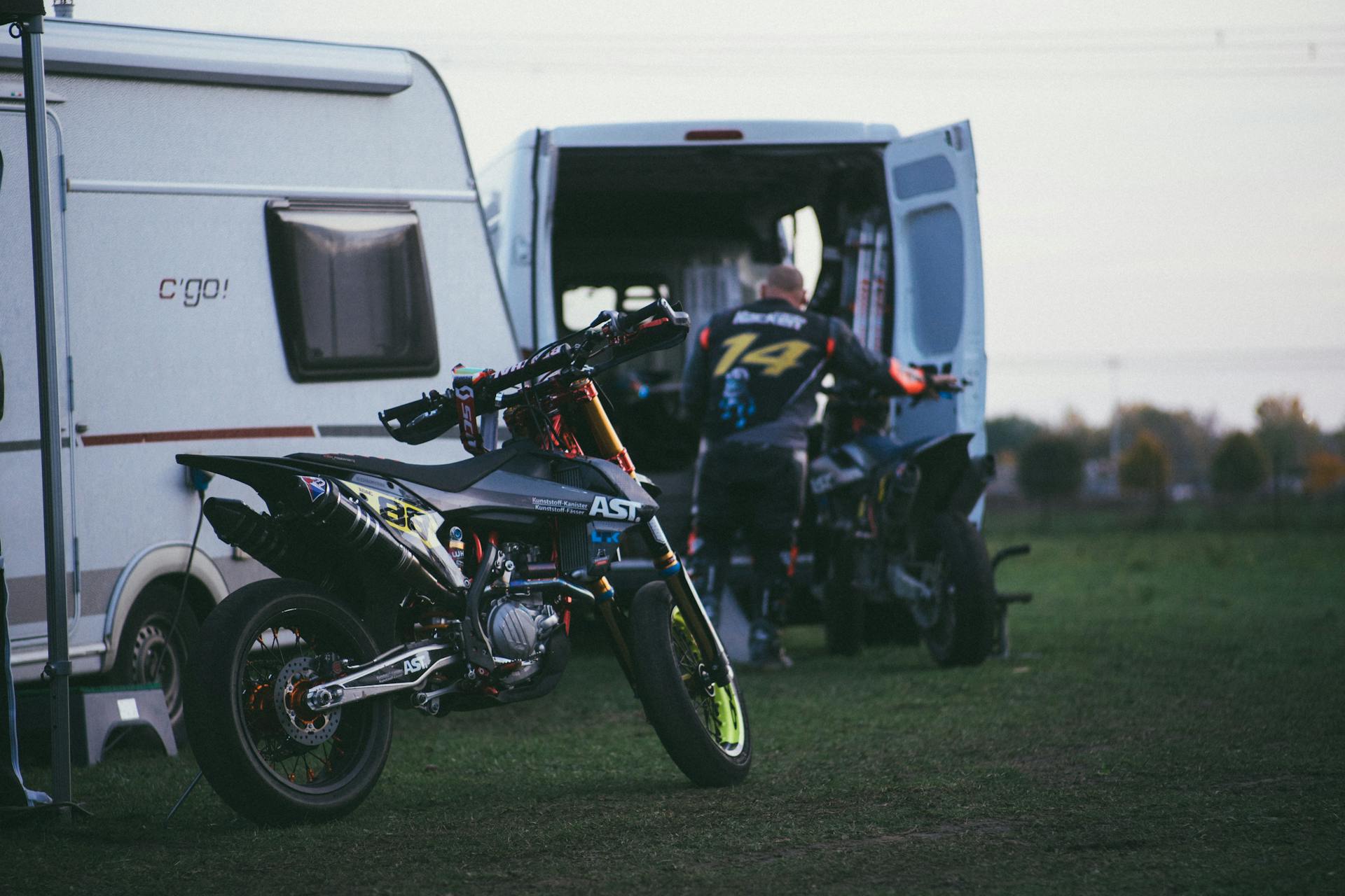 Parked off-road motorcycle by a van and camper at a scenic campsite.
