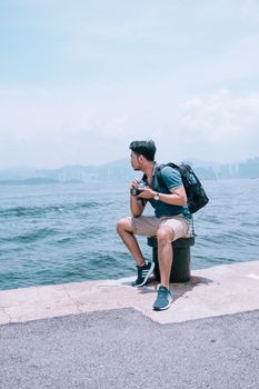 A young traveler with a camera sits by the ocean, capturing scenic views.