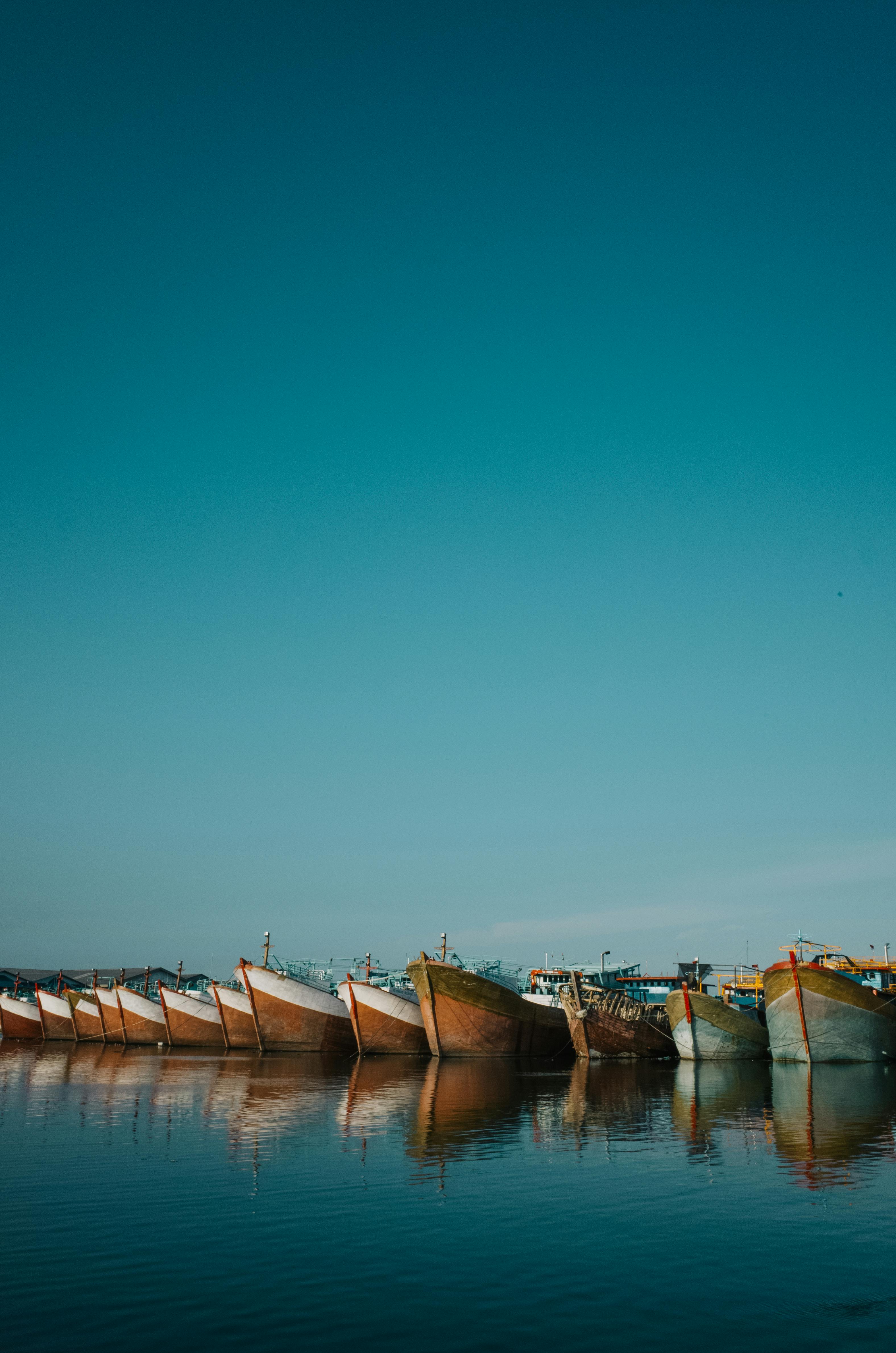 Free A peaceful view of boats lined up on calm water under a clear blue sky. Stock Photo