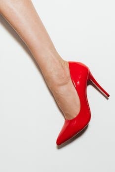 A stylish red high heel on a woman's foot against a white background, showcasing elegance and fashion.