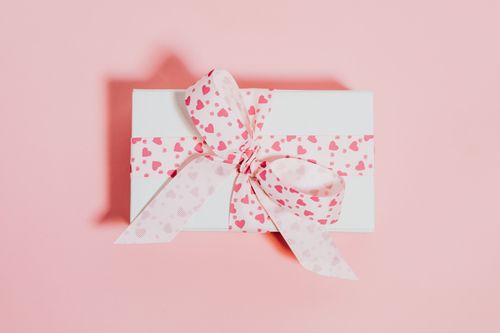 Free White gift box with pink heart-patterned ribbon on a soft pink background, ideal for celebrations. Stock Photo