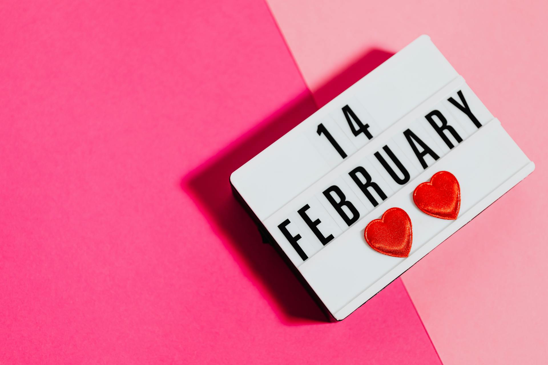 A Light Up Message Board with 14 February Written on It on a Pink Background