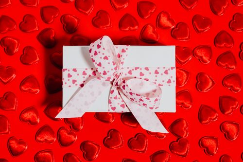Free Top view of a gift box with heart pattern ribbon on a red background with heart shapes. Stock Photo