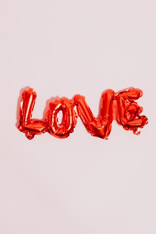 Free Shiny red balloon letters spelling LOVE on a soft pink background for romantic decoration. Stock Photo