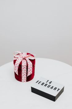 一个浪漫的红色礼品盒旁系着蝴蝶结，旁边还放着一本标有2月14日的日历