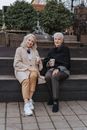 两名高级女性坐在台阶上，在户外休闲的环境中微笑地喝着咖啡