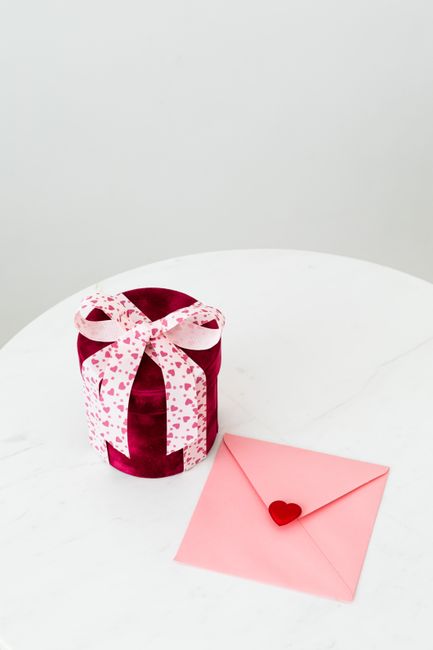 A charming round gift with heart-patterned ribbon alongside a pink envelope with a heart seal, perfect for Valentine's.