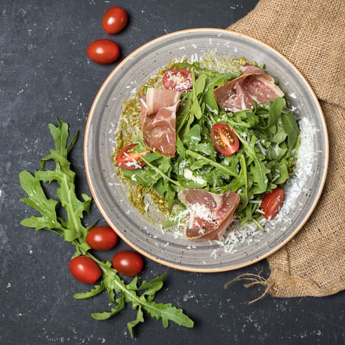 Free Delicious arugula salad topped with prosciutto, cherry tomatoes, and parmesan cheese. Stock Photo
