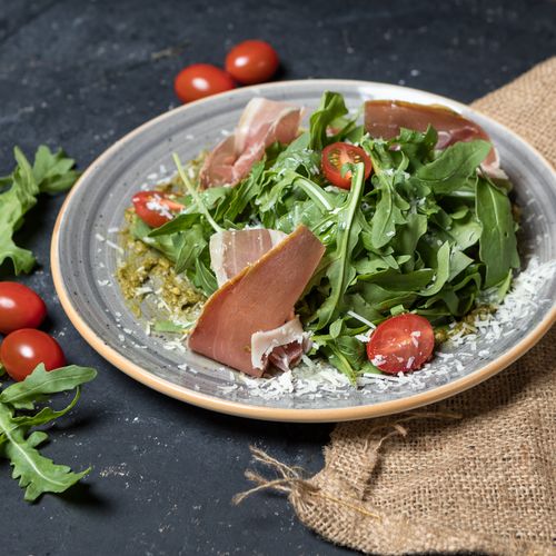 Free Fresh arugula salad topped with prosciutto, cherry tomatoes, and Parmesan cheese. Perfect for a gourmet meal. Stock Photo