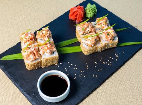 Close-up of sushi rolls with garnishes on slate plate, served with soy sauce.