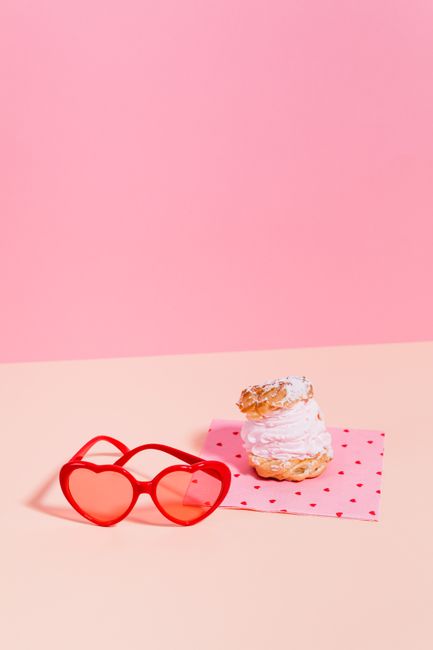 Heart-shaped sunglasses and a cream puff on a pink background, evoking sweetness and love.