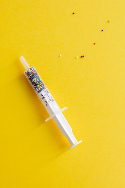 A syringe filled with colorful sprinkles on a bright yellow background, creating a playful and conceptual image.