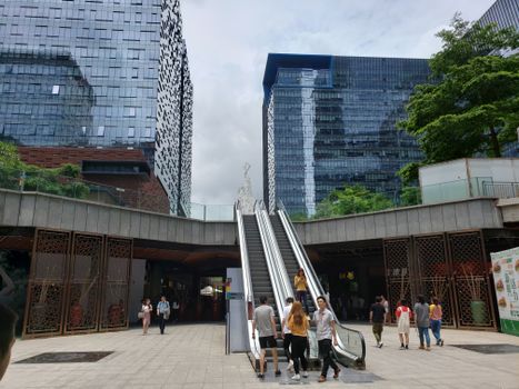 Urban city scene in China with people on escalators amid modern glass buildings.