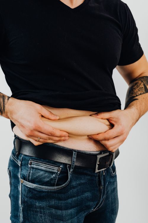 Free Close-up of a man in a black shirt displaying tattoos while pinching his belly skin. Stock Photo