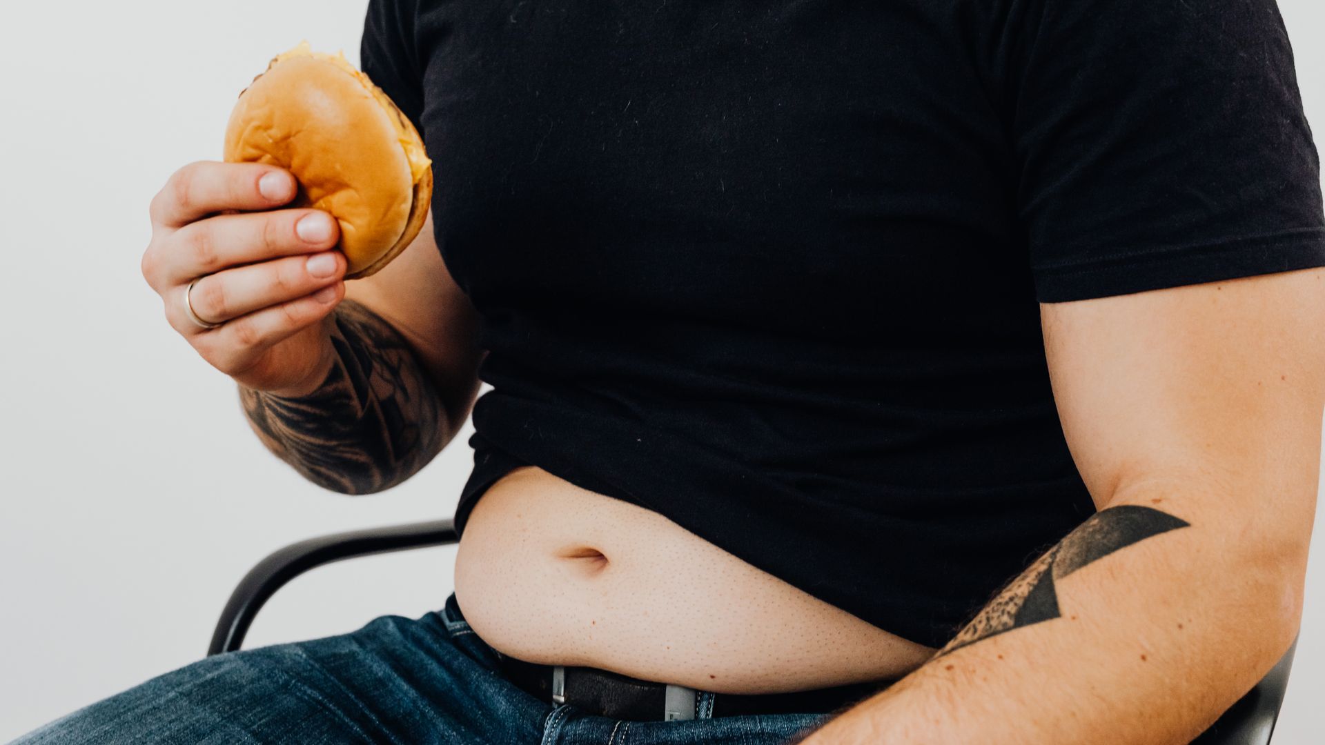 Modafinil Appetite Loss: Understanding the Effect Close-up of a man holding a burger, showcasing his torso and tattooed arm. Casual and relaxed setting — modafinil appetite loss