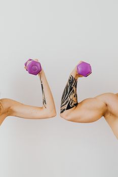 Close-up of tattooed arms holding purple dumbbells showcasing strength and fitness.