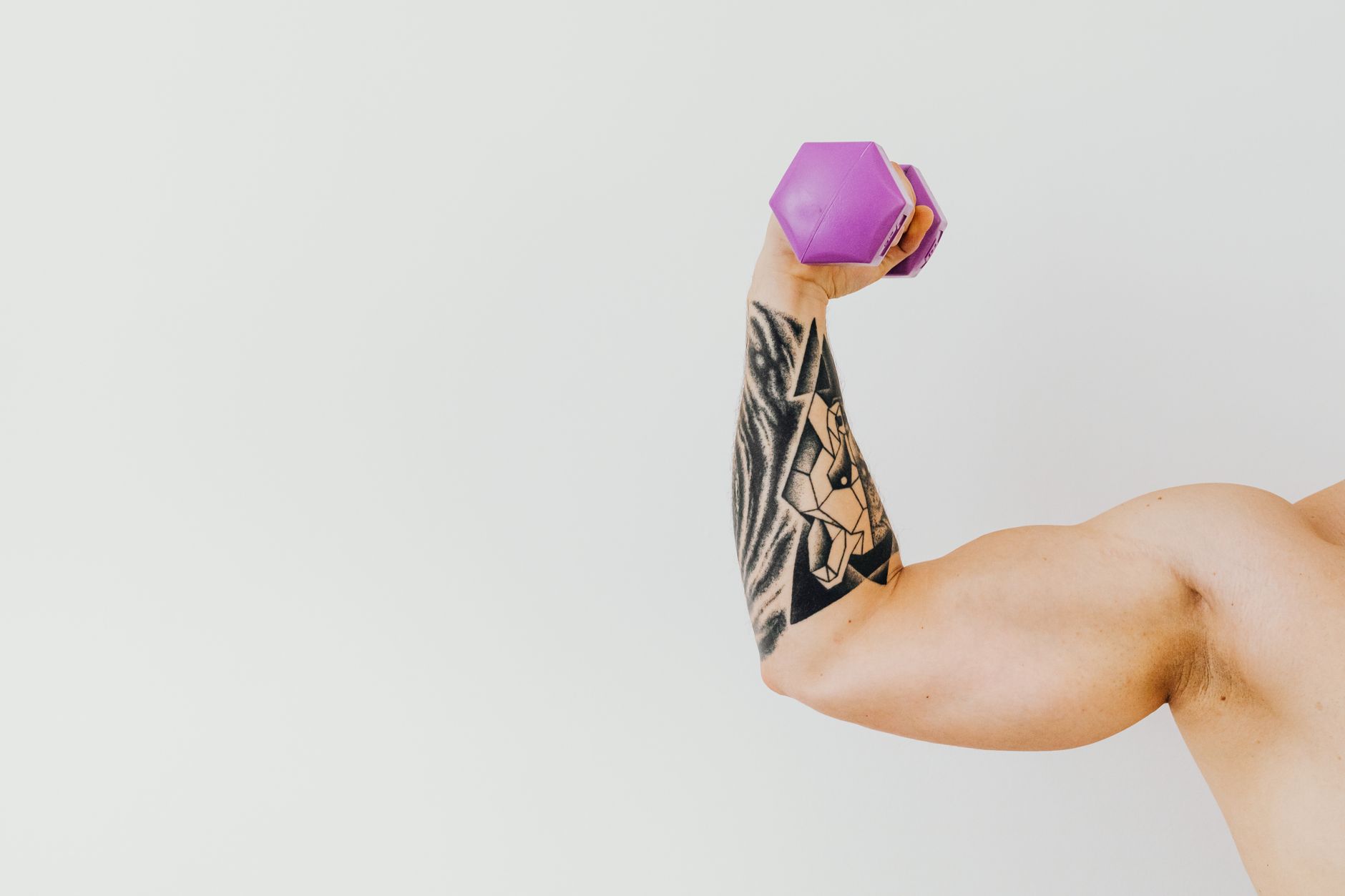 A tattooed arm lifting a purple dumbbell, showcasing strength and fitness.