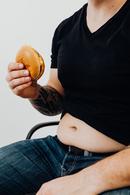 Free Man wearing black shirt sits holding a burger, highlighting casual eating habits. Stock Photo