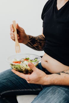 Person holding a bowl of salad with visible tattoos, highlighting healthy eating with personal style.