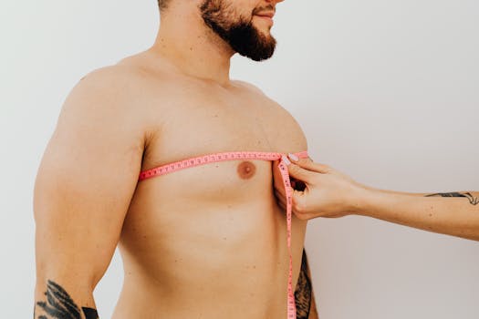 Close-up of a man's chest being measured with a pink measuring tape against a white background.