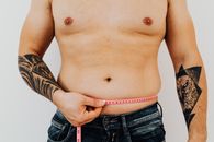 一名有纹身的男子正在用胶带测量腰围，以关注健身或减肥效果