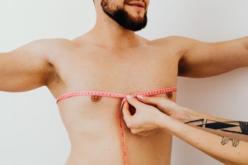 Free A shirtless man has his chest measured using a pink tape measure indoors. Stock Photo