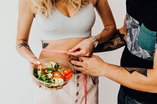 A couple measuring waistline with a tape and holding a fresh salad bowl, focusing on fitness and weight loss.