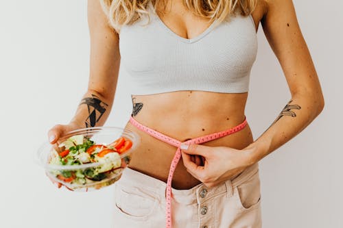 Free Woman in Sports Bra Holding a Measuring Tape and Bowl of Salad Stock Photo